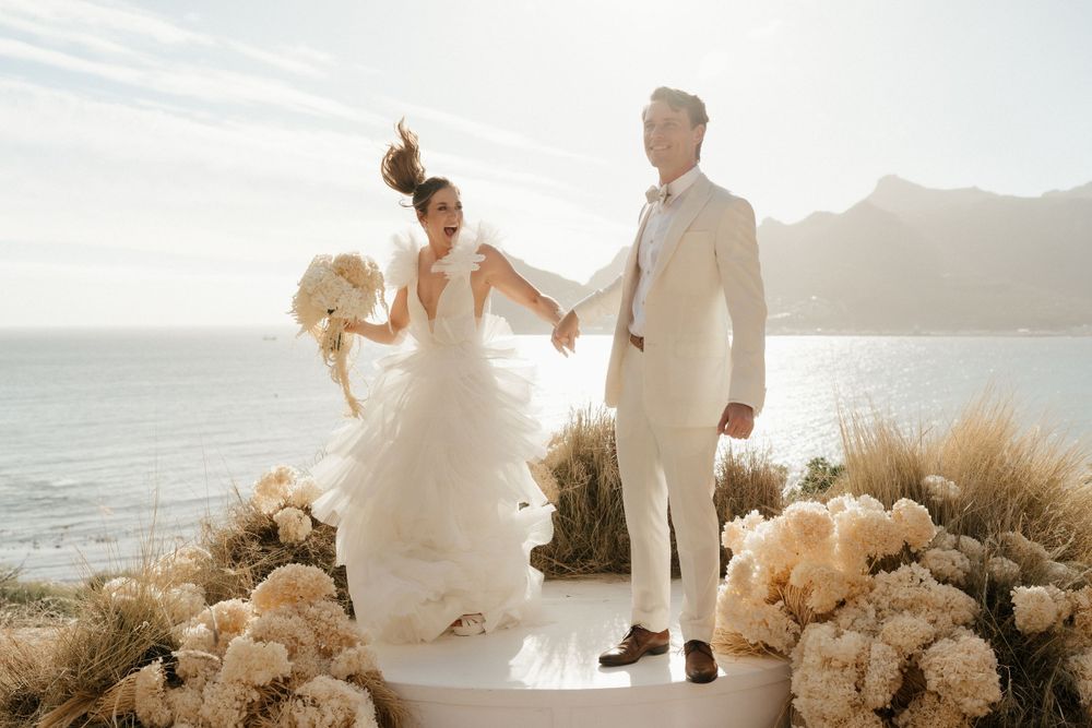 Scenic coastal wedding ceremony with dried pampas grass decorations at sunset.