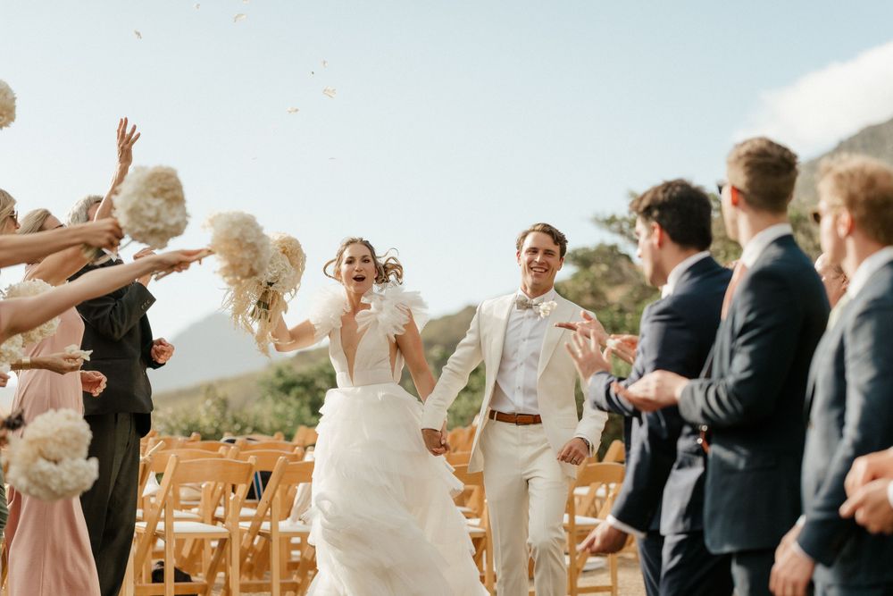 Wedding celebration with guests throwing flower petals in an outdoor mountain setting.