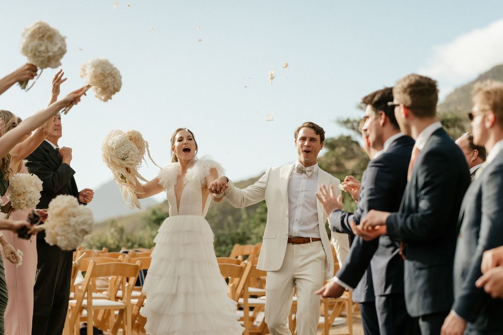 Wedding guests toss flower petals during an outdoor mountain ceremony.