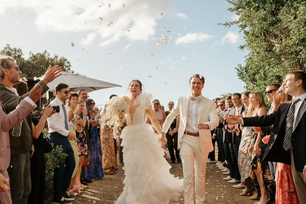 Wedding guests throwing confetti over couple during outdoor ceremony exit.