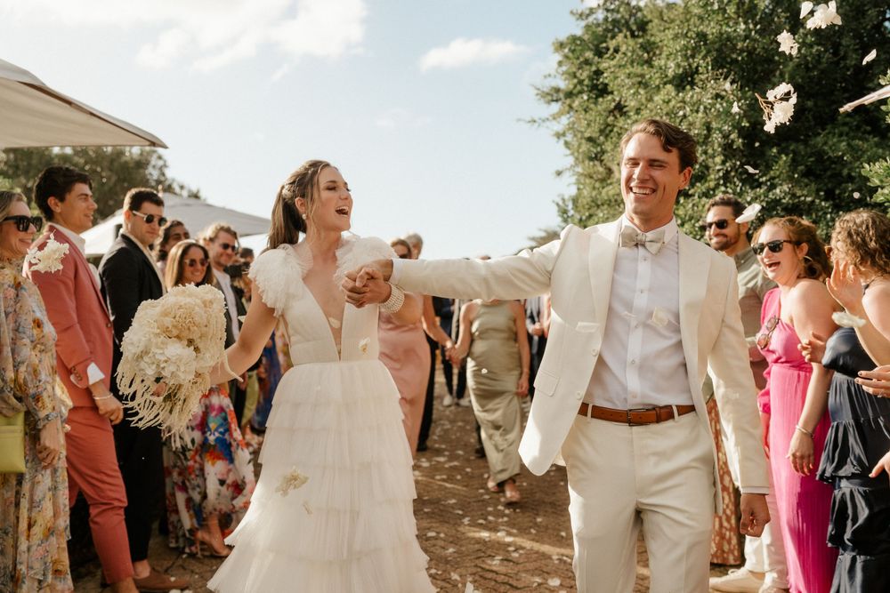 Newlyweds exit wedding ceremony along pathway lined with celebrating guests.