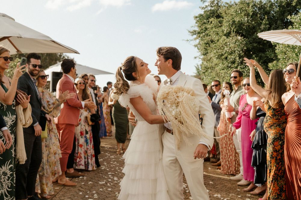 Wedding couple shares intimate moment while guests celebrate at outdoor reception.