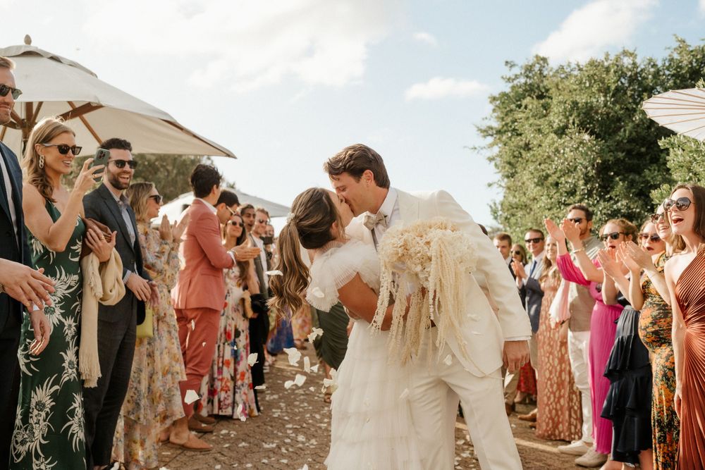 A couple shares their first dance at an outdoor wedding celebration surrounded by guests and white umbrellas.