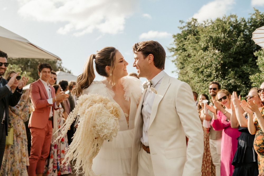 Wedding celebration outdoors with guests clapping as couple shares a special moment.