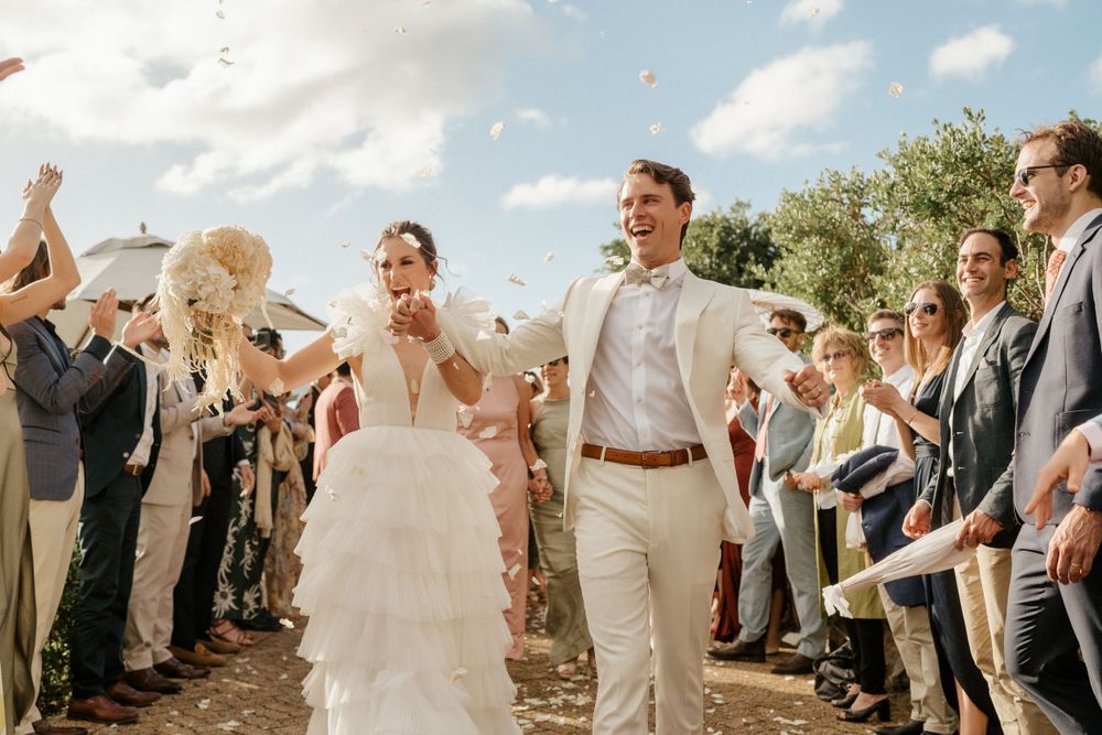 Wedding couple celebrating with guests throwing confetti outdoors.