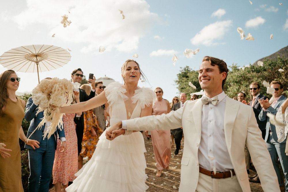 Wedding celebration on sunny beach with guests throwing confetti as couple dances.