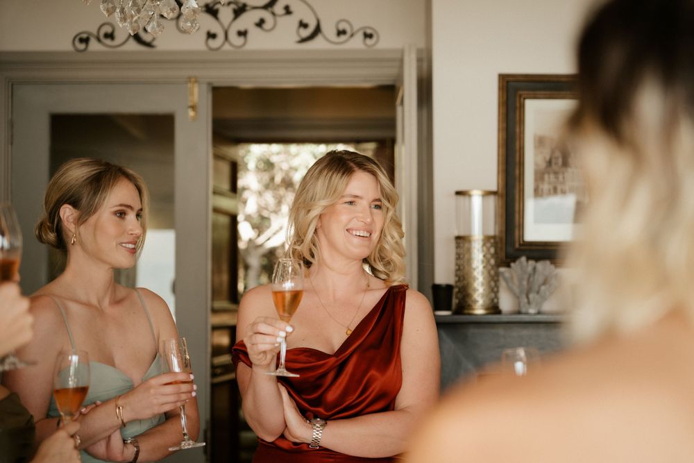Friends in elegant attire share drinks and laughter during a wedding celebration.