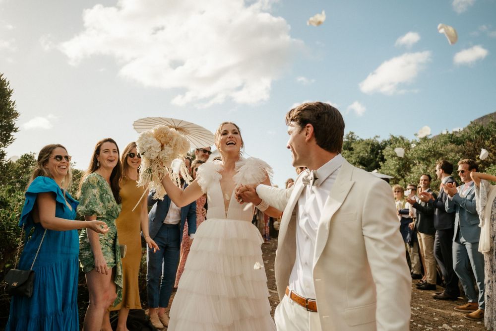 Wedding celebration on sunny hillside with guests in colorful attire watching couple's first dance.