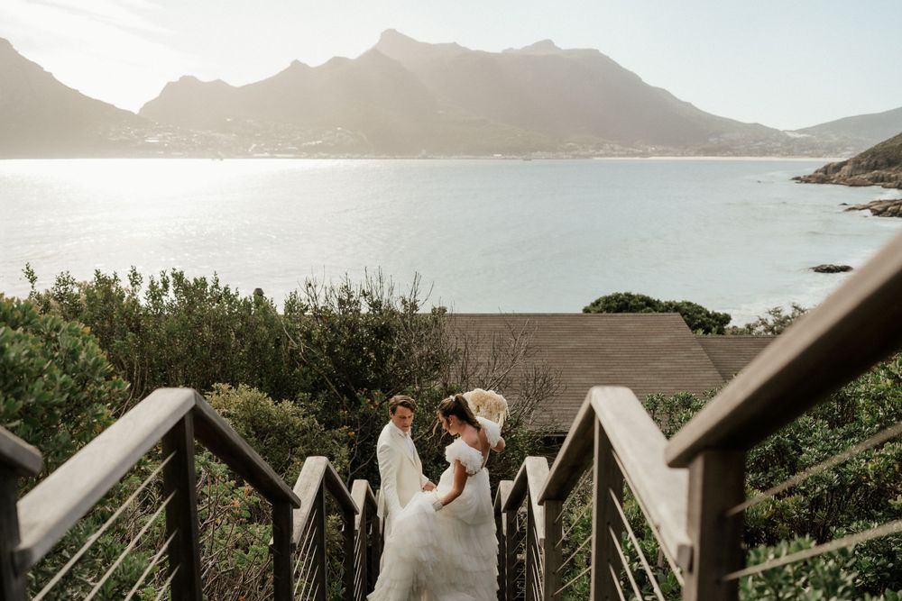Couple descends scenic coastal stairway with dramatic mountain views at sunset.