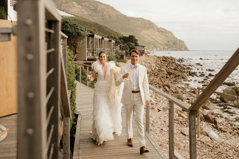A couple walking along a coastal boardwalk during their wedding celebration.