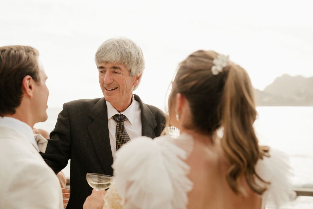 Intimate conversation during outdoor wedding reception by the water.