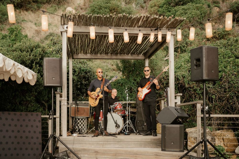 Musicians perform on a rustic outdoor stage with sound equipment and lantern decorations.