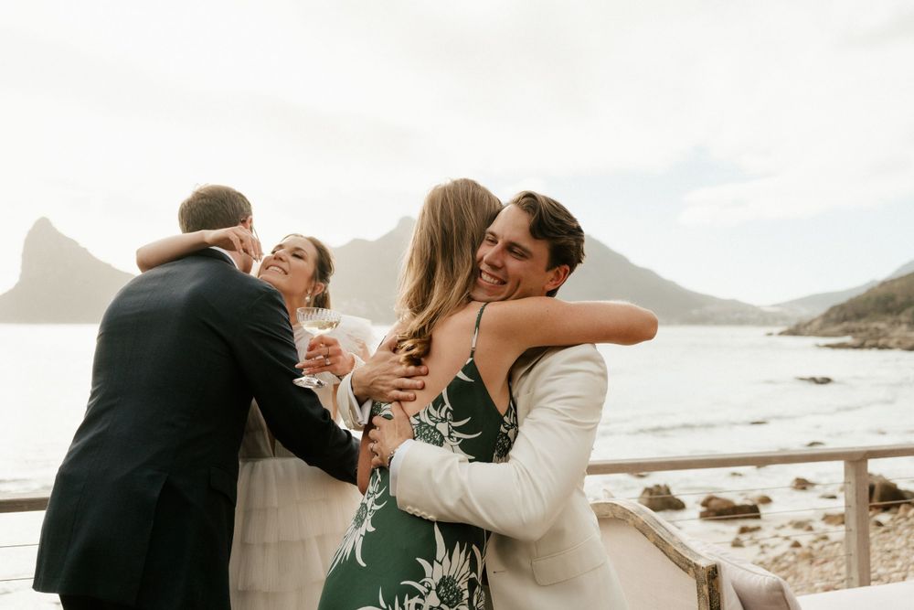 Wedding guests embrace and celebrate on scenic coastal overlook.