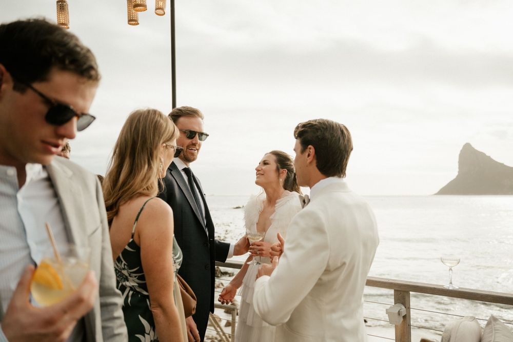 Wedding guests mingle and chat during coastal outdoor reception.