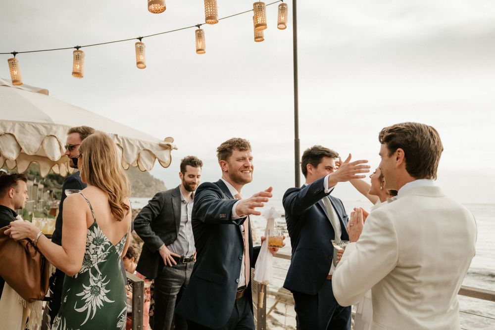 Wedding guests mingling and chatting under string lights at outdoor reception.