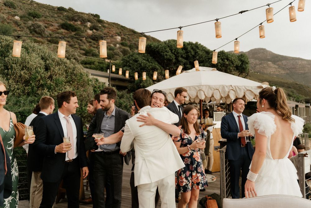 Wedding celebration with string lights and lanterns as guests dance outdoors at sunset.