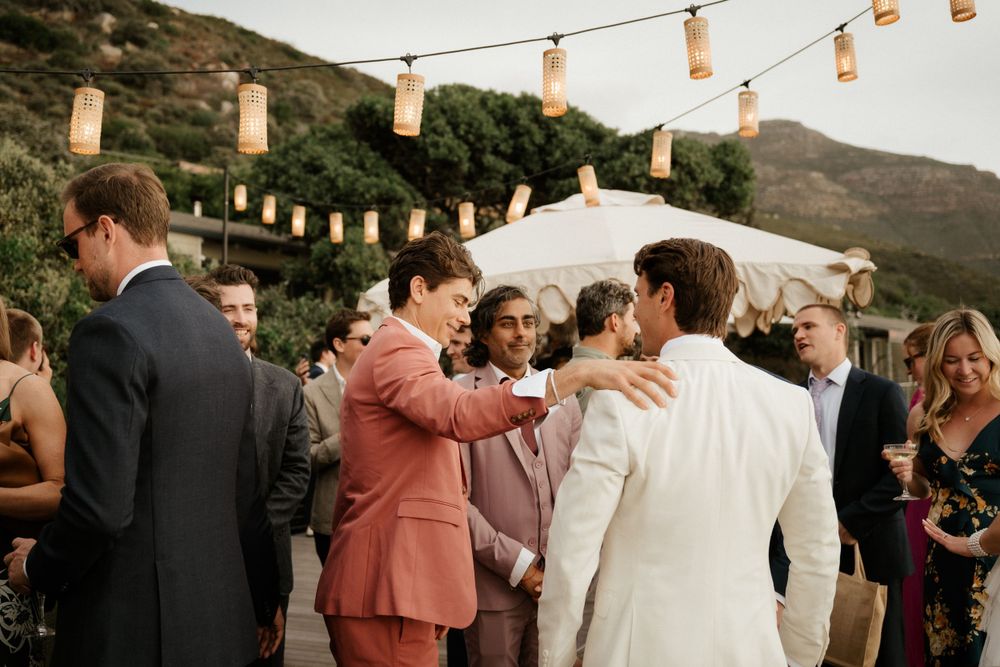 Wedding reception with string lights and guests mingling outdoors at sunset.