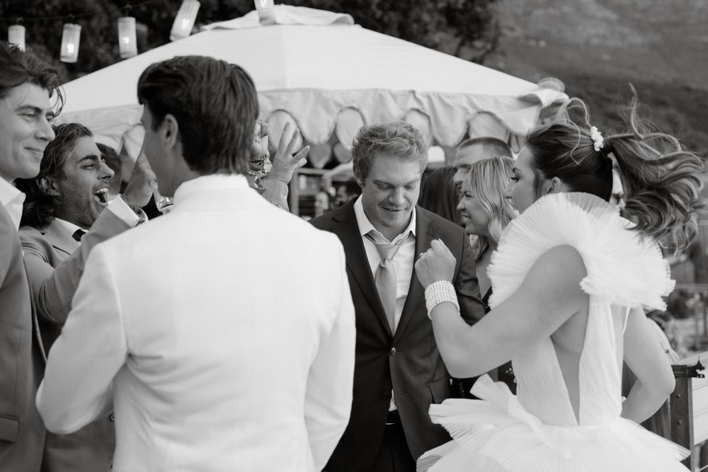 Black and white photo of joyful wedding celebration with guests dancing outdoors.