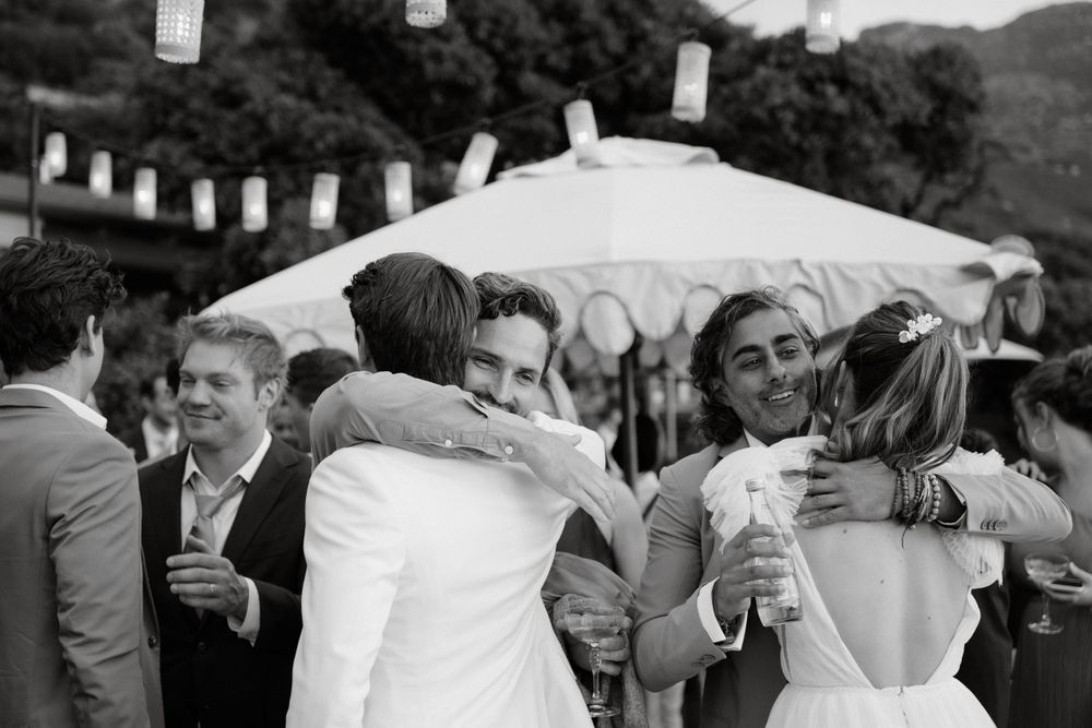 Black and white photo of wedding guests embracing during reception with paper lanterns overhead.