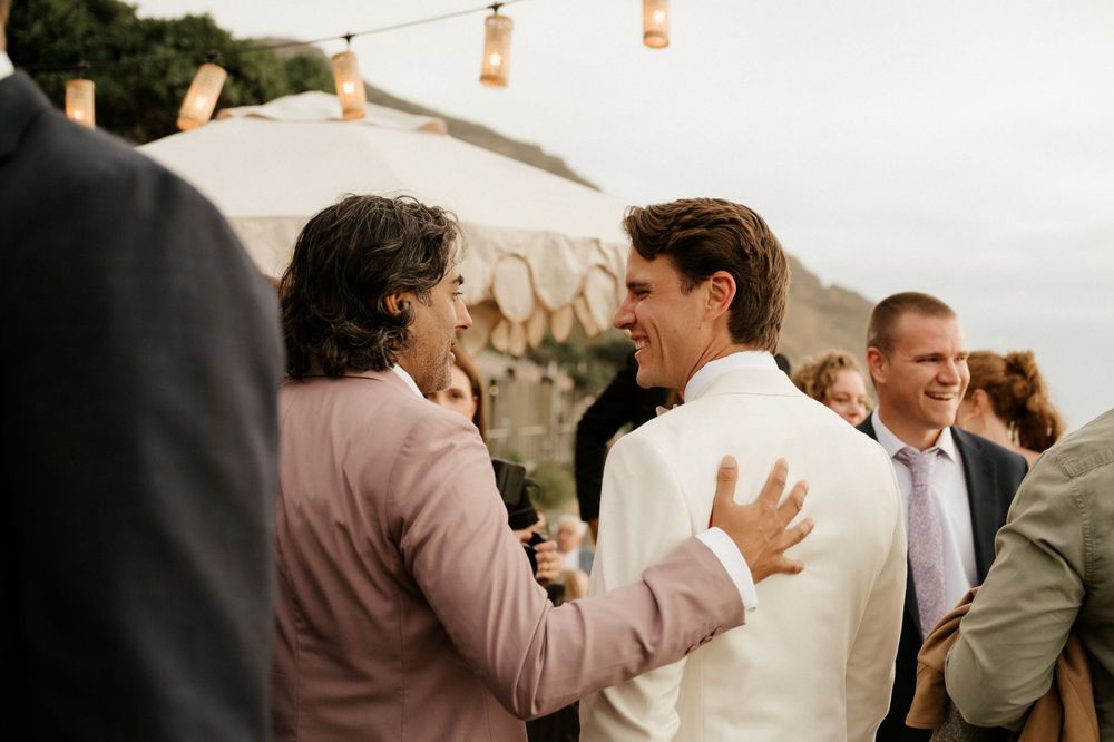 Wedding guests mingling at outdoor cocktail reception against mountain landscape.