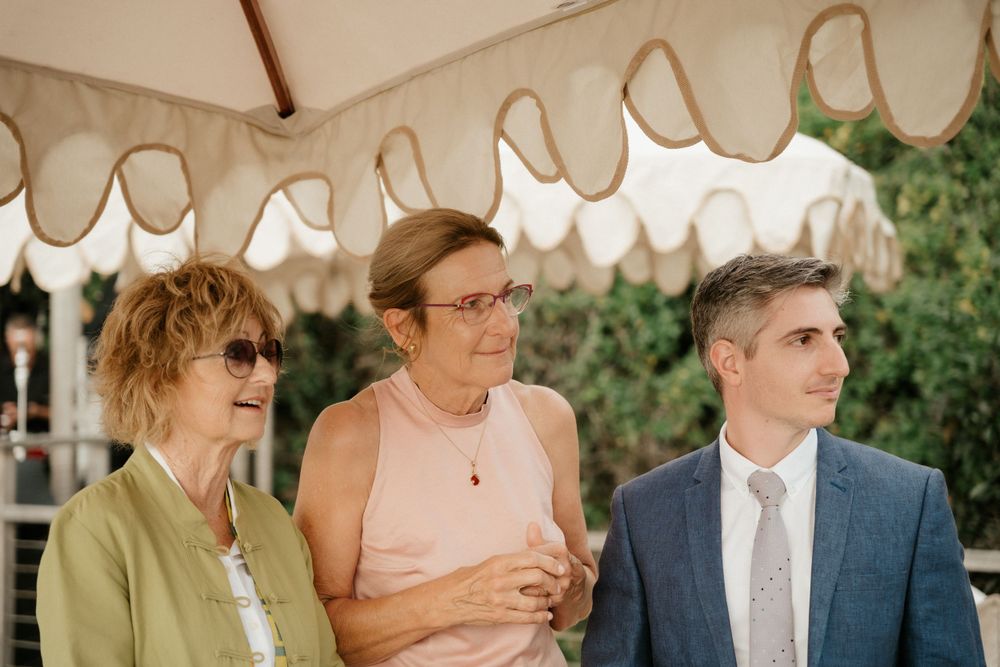 Three people sitting under a white scalloped awning at an outdoor event.