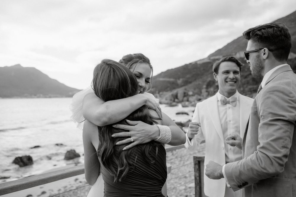 Black and white photograph of emotional embrace during coastal wedding celebration.