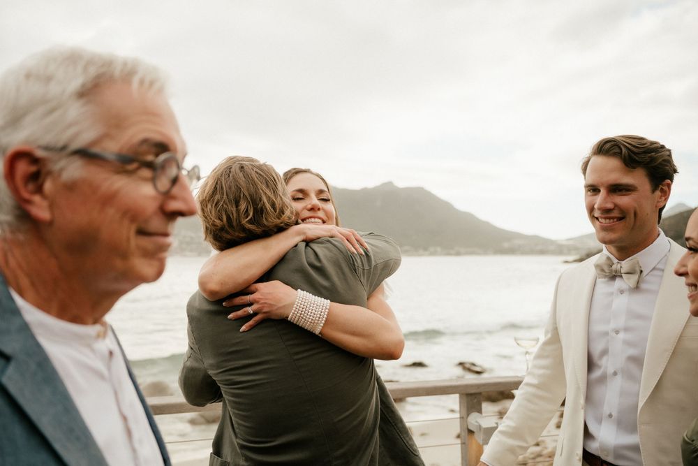 Emotional moment between wedding guests hugging with mountain scenery in background.