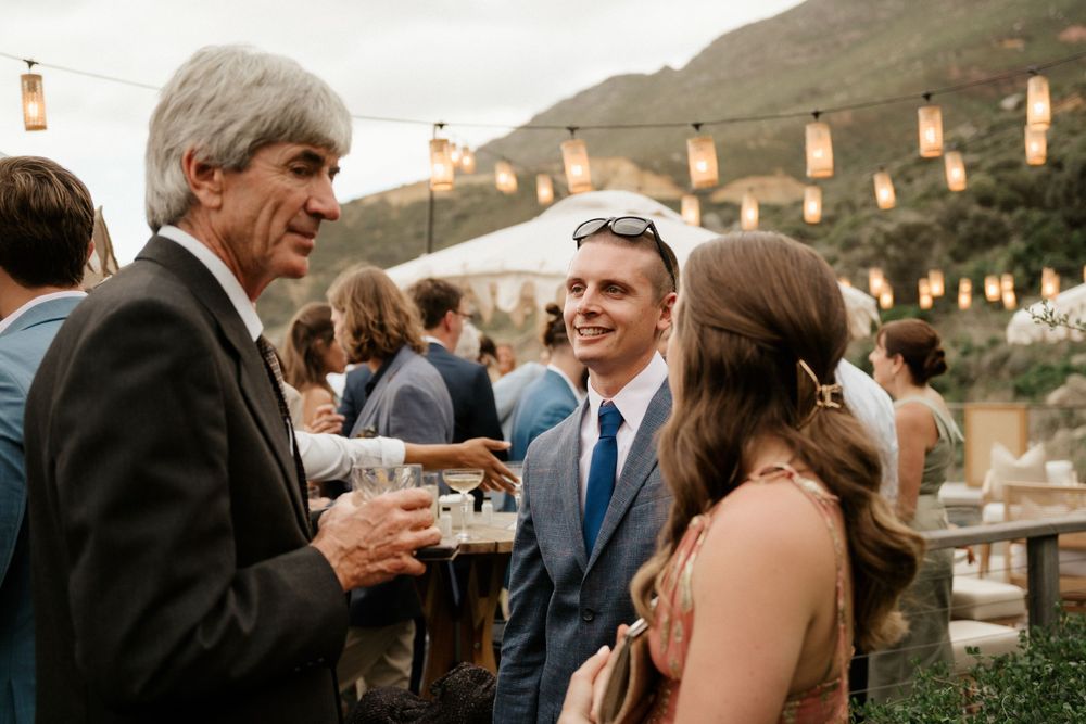 Wedding guests enjoying conversation during an outdoor reception with string lights and mountain views.