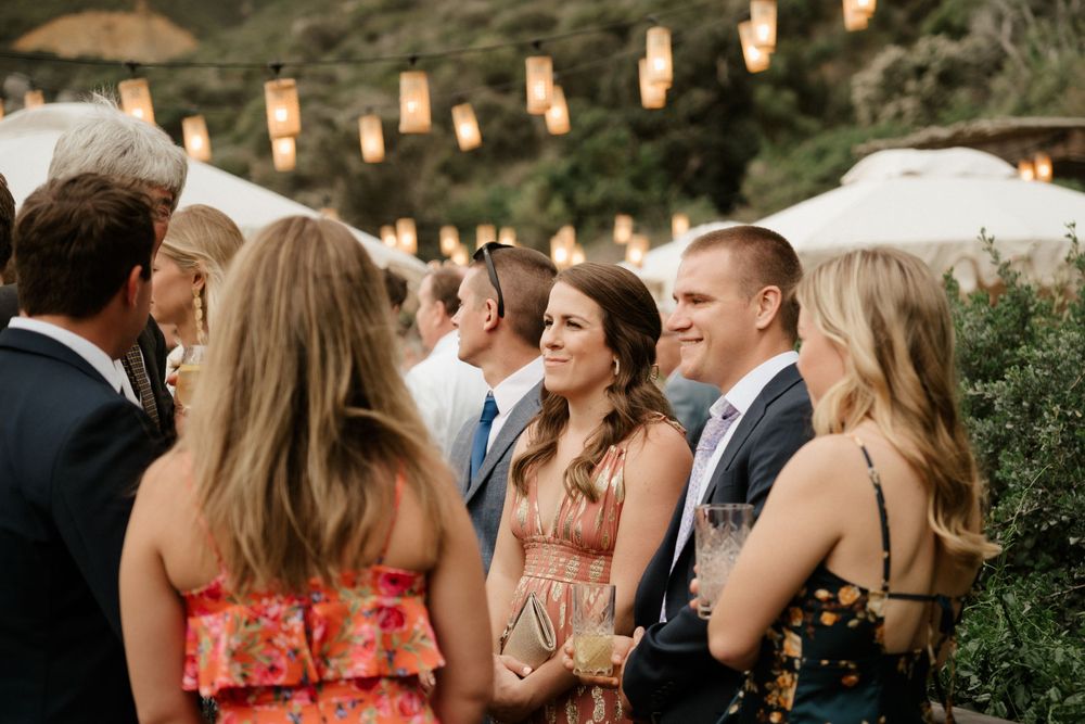 Wedding guests mingling outdoors under string lights at dusk during a celebration.