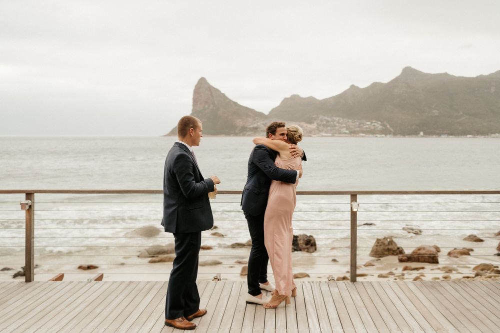Intimate wedding ceremony on oceanfront deck with mountain backdrop.