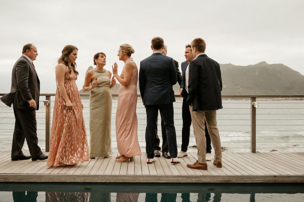 Wedding party stands on a wooden dock with mountain views in elegant attire.