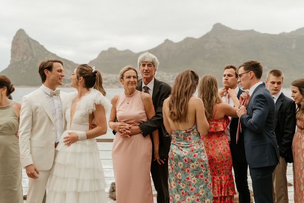 Wedding guests mingle during a cocktail hour with dramatic mountain peaks in the background.