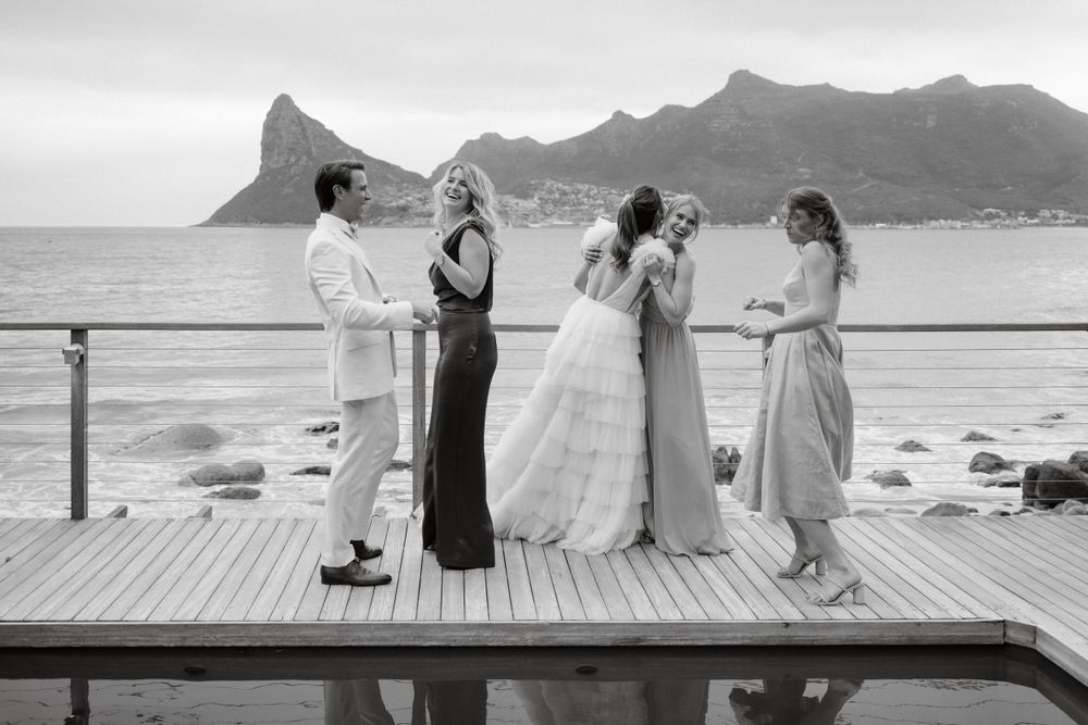 Wedding party gathered on a wooden deck overlooking dramatic coastal mountains in black and white.