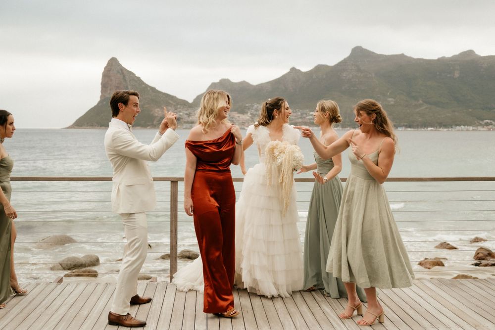 Wedding group in formal attire sharing candid moment on oceanfront deck.