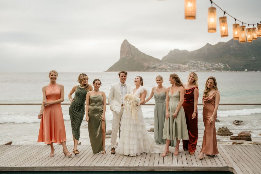 Wedding party poses on a deck with dramatic mountain and ocean views at sunset.