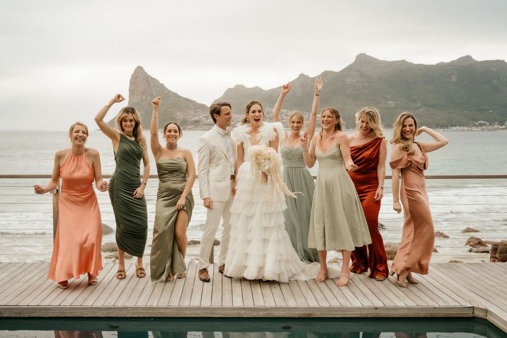 Wedding party poses on wooden deck with mountain landscape in background.
