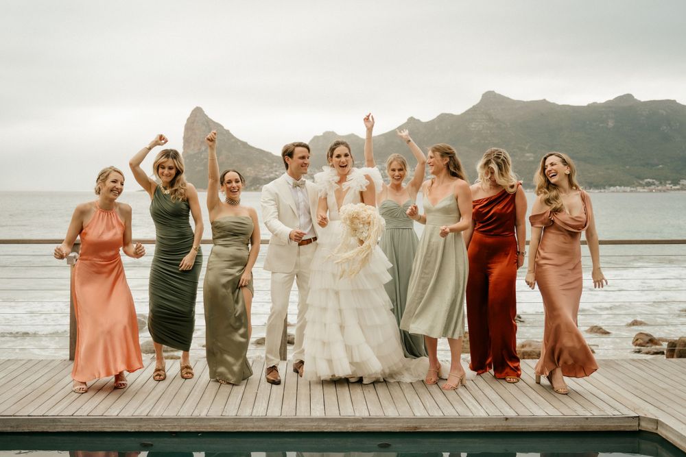 Wedding party poses together on wooden deck with mountain landscape behind them.