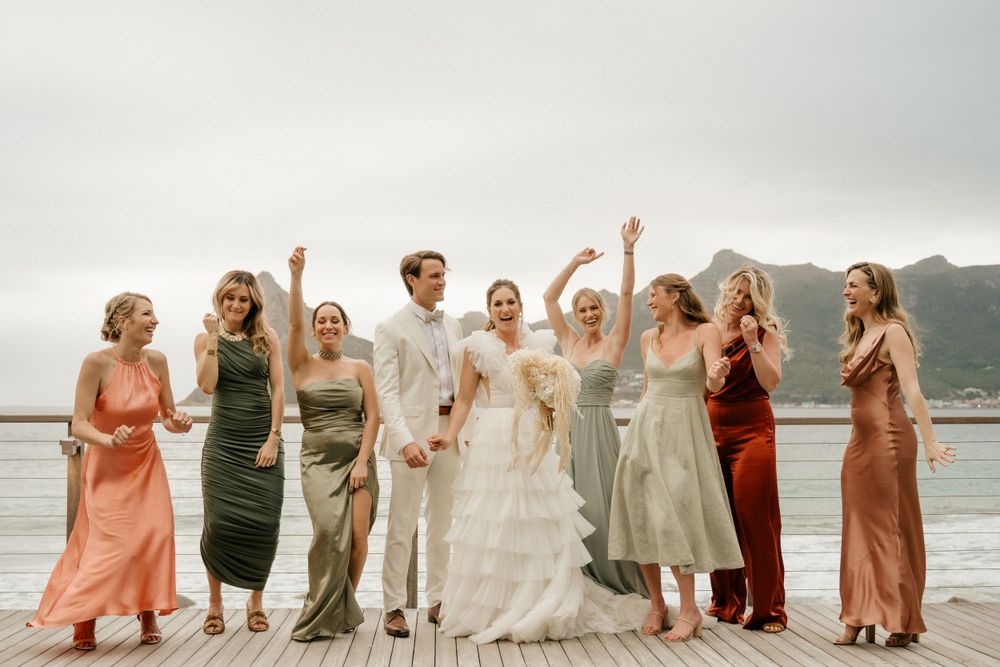 Wedding party in colorful dresses celebrates on a deck overlooking mountain scenery.