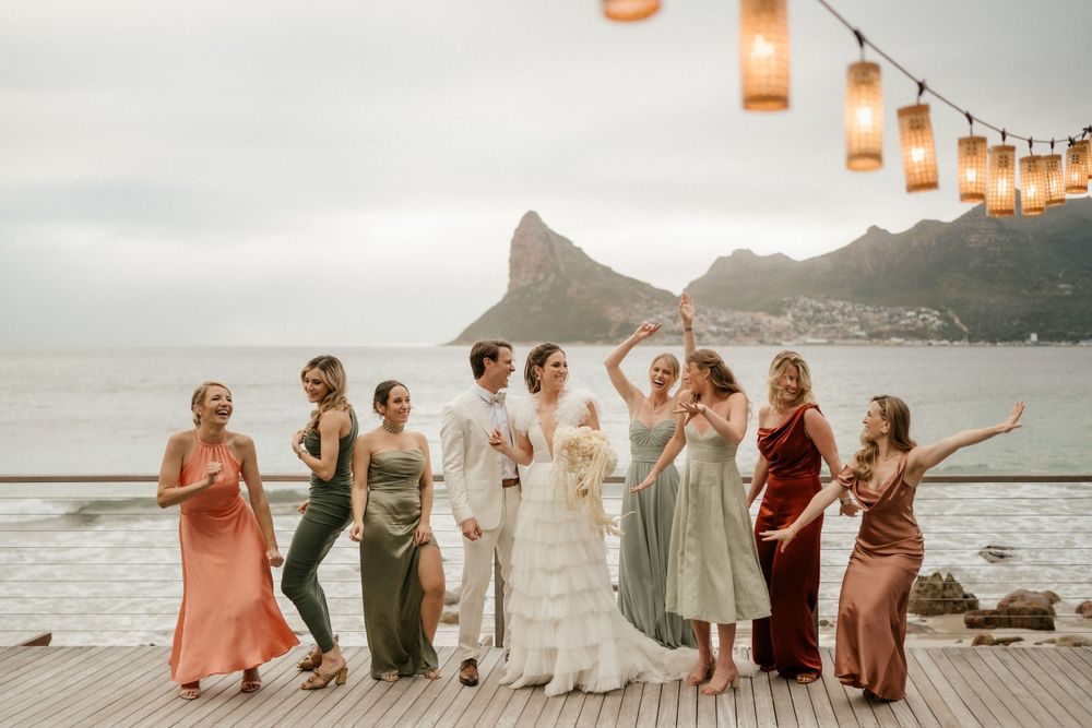 Wedding party posing on a wooden deck overlooking dramatic mountain peaks and ocean views.