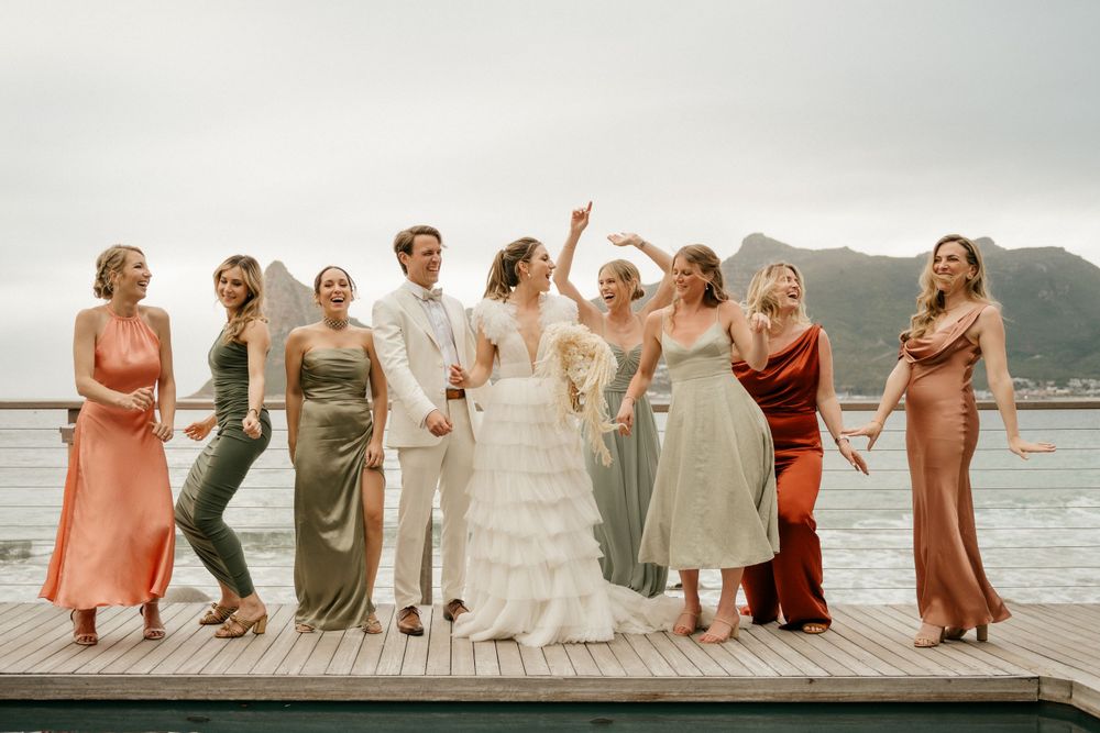 Wedding party poses on a wooden dock with ocean and mountain views.