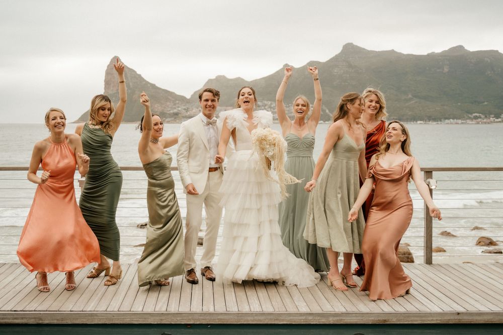Wedding party celebrates on a wooden deck overlooking a scenic mountain and ocean landscape.