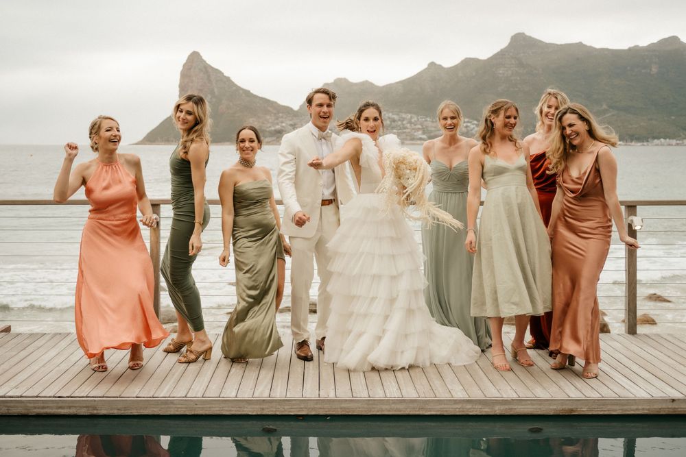 Wedding party poses together on a wooden deck with mountain and ocean backdrop.