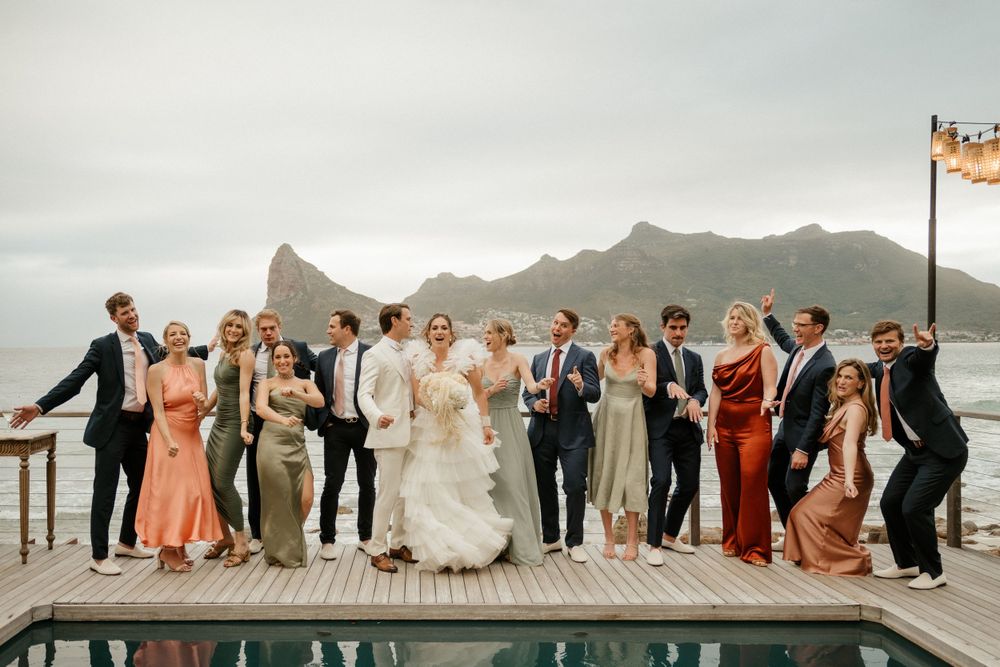 Wedding party celebrating on a deck with dramatic mountain and ocean views in the background.