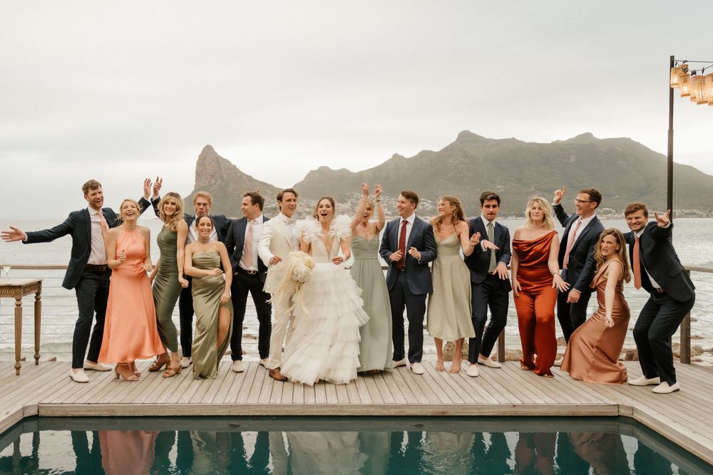 Wedding party celebrating by a poolside with mountain backdrop in elegant attire.