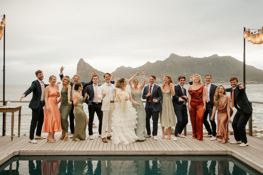 Wedding party poses on deck with mountain backdrop and pool.