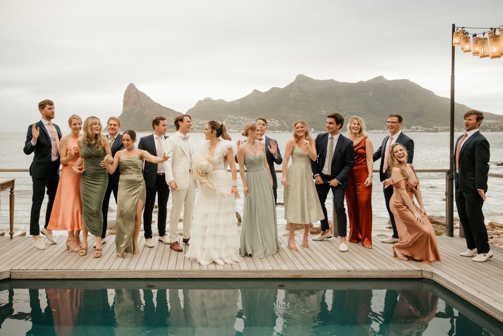 A wedding party poses together on a deck overlooking mountains and water.