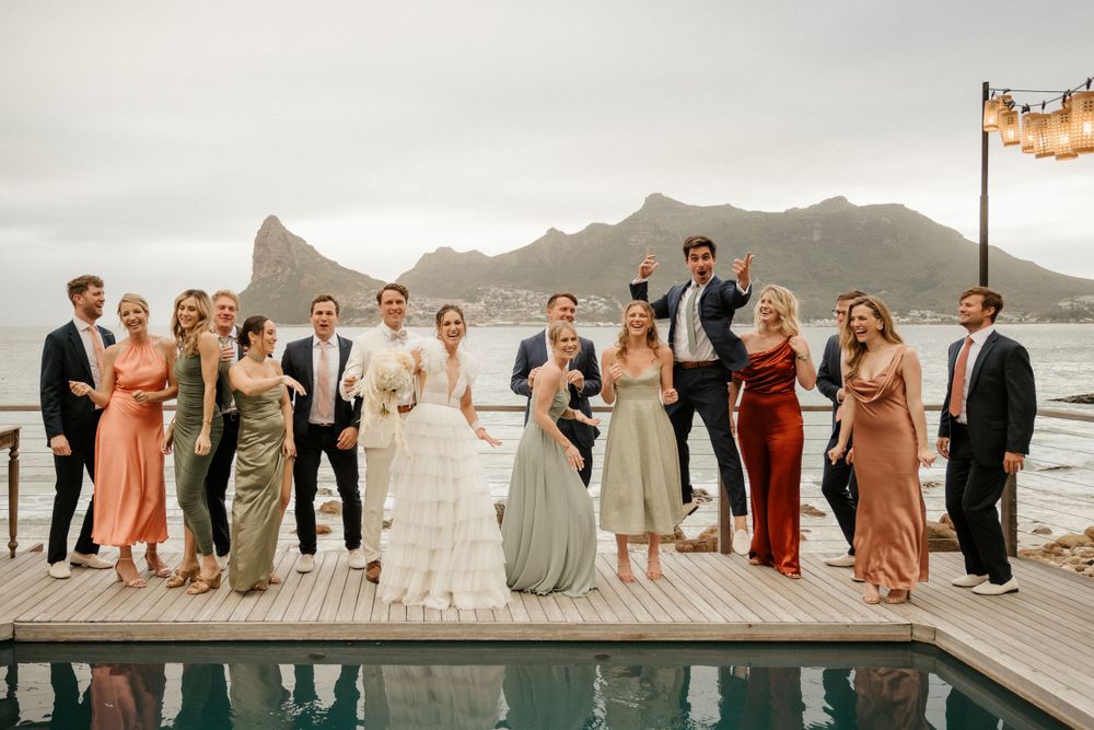 Wedding party poses by mountain lake with bridal couple and attendants in formal attire.