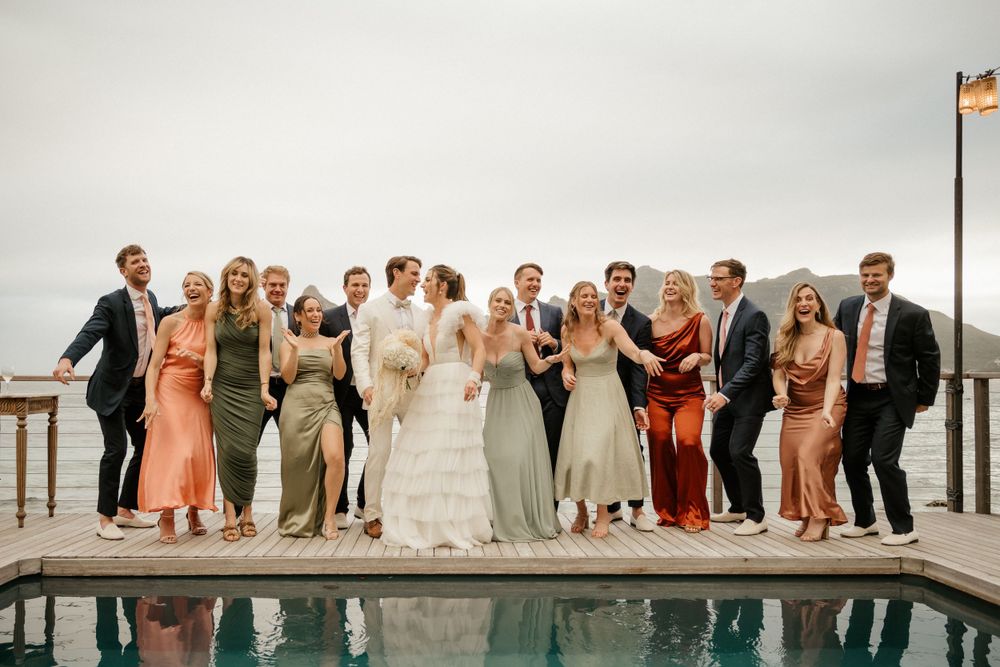 Wedding party poses together on a wooden deck with mountain backdrop and reflective pool.