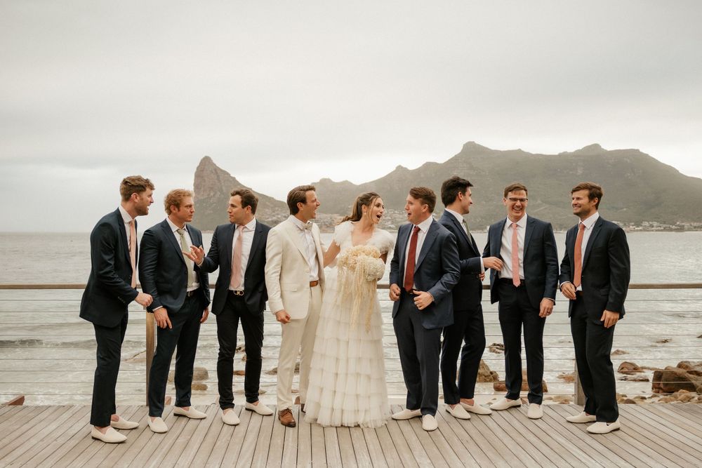 Wedding party in formal attire gathered on wooden deck with mountain view.
