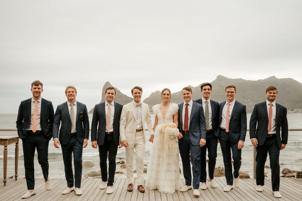 Wedding party in formal attire poses on deck overlooking coastal mountains.